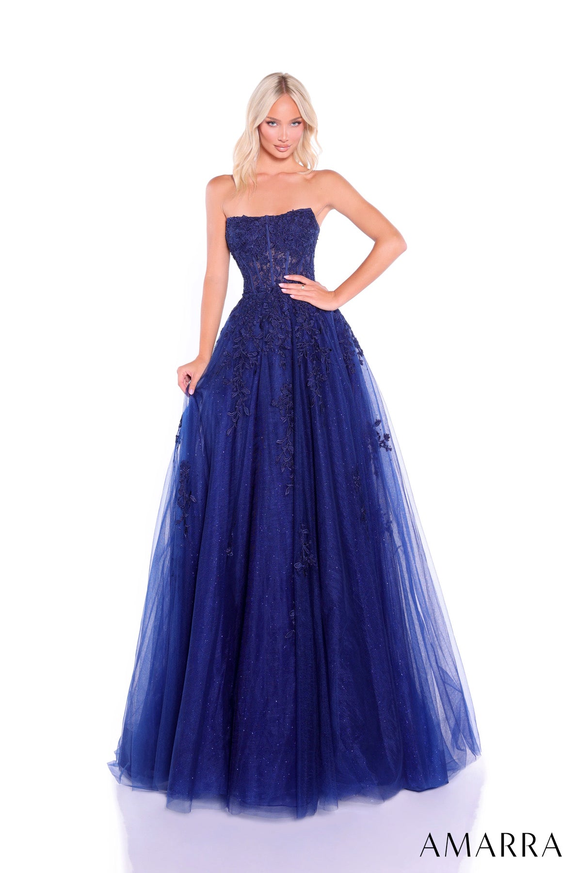 Woman wearing a strapless, long, blue evening gown with lace details on a white background. Brand 'AMARRA' visible. THE BRIDAL COMPANY