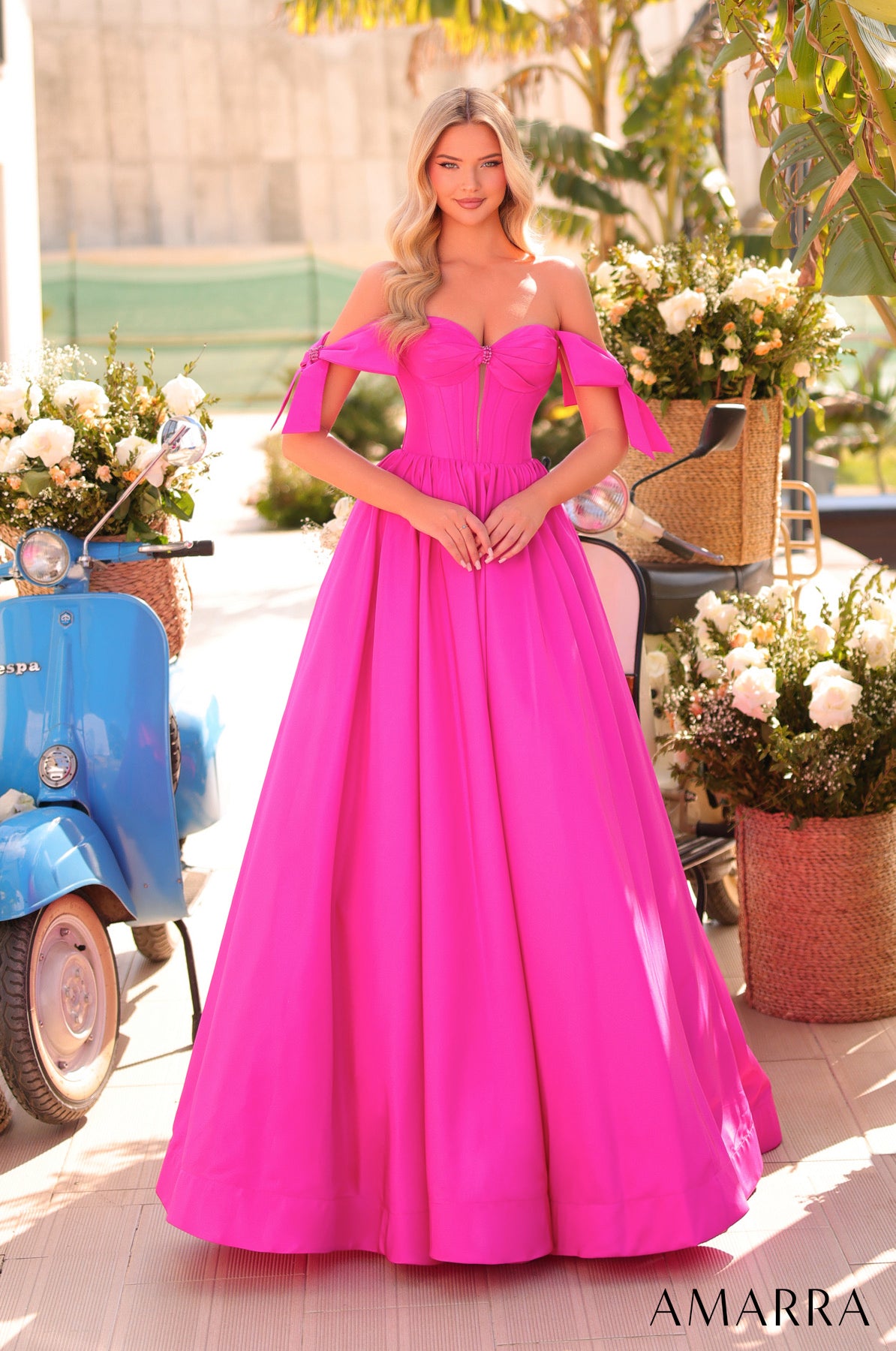 Woman in a bright pink evening gown standing outdoors with flowers and a scooter in the background, brand 'AMARRA' visible.