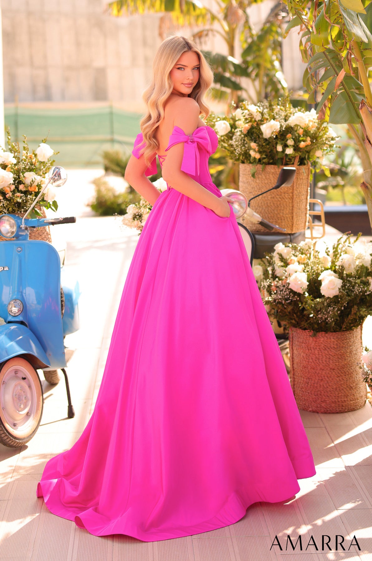 Woman in a bright pink dress standing outdoors with flowers and a scooter in the background, brand 'AMARRA' visible.