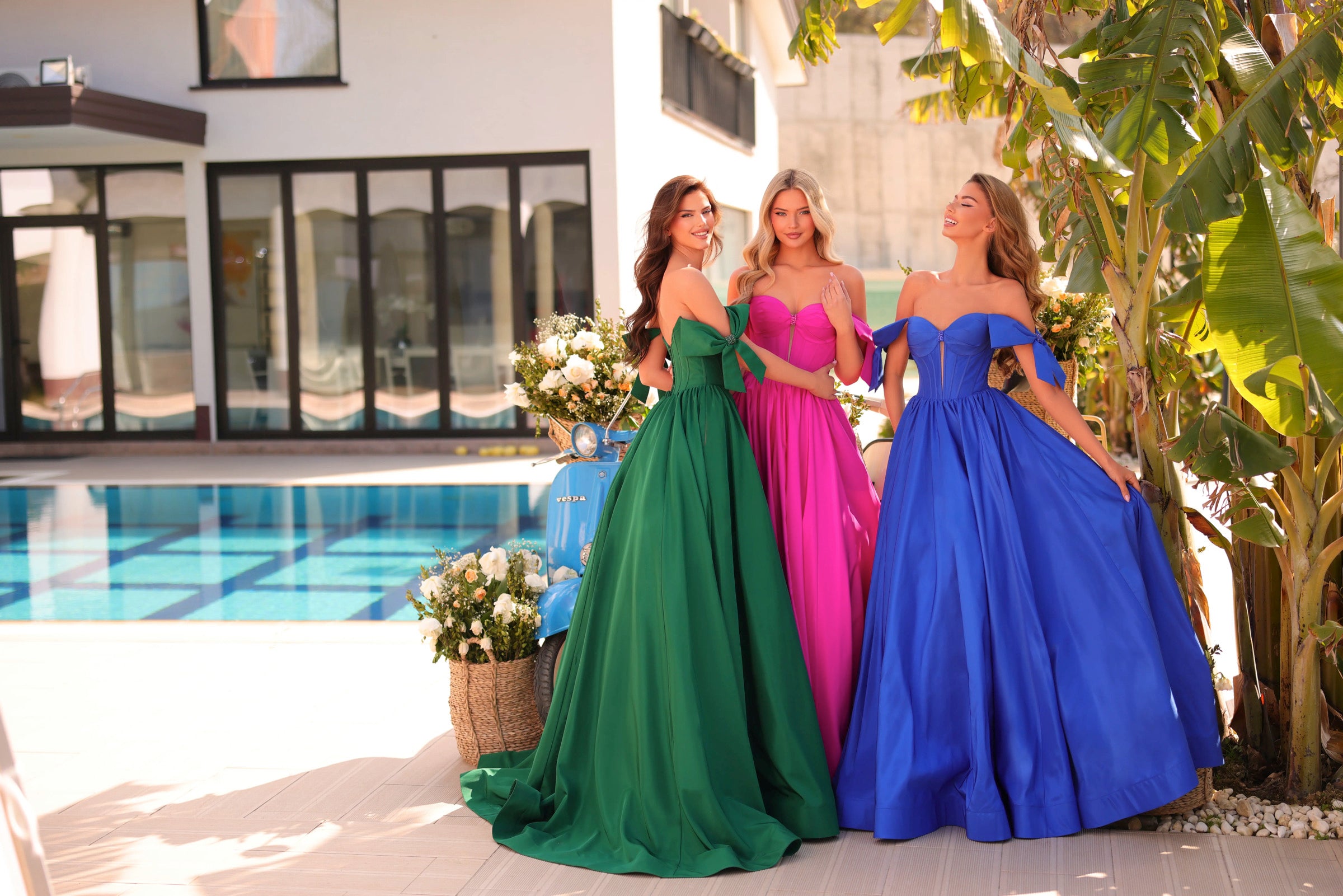 Three women in colorful evening gowns standing by a poolside.