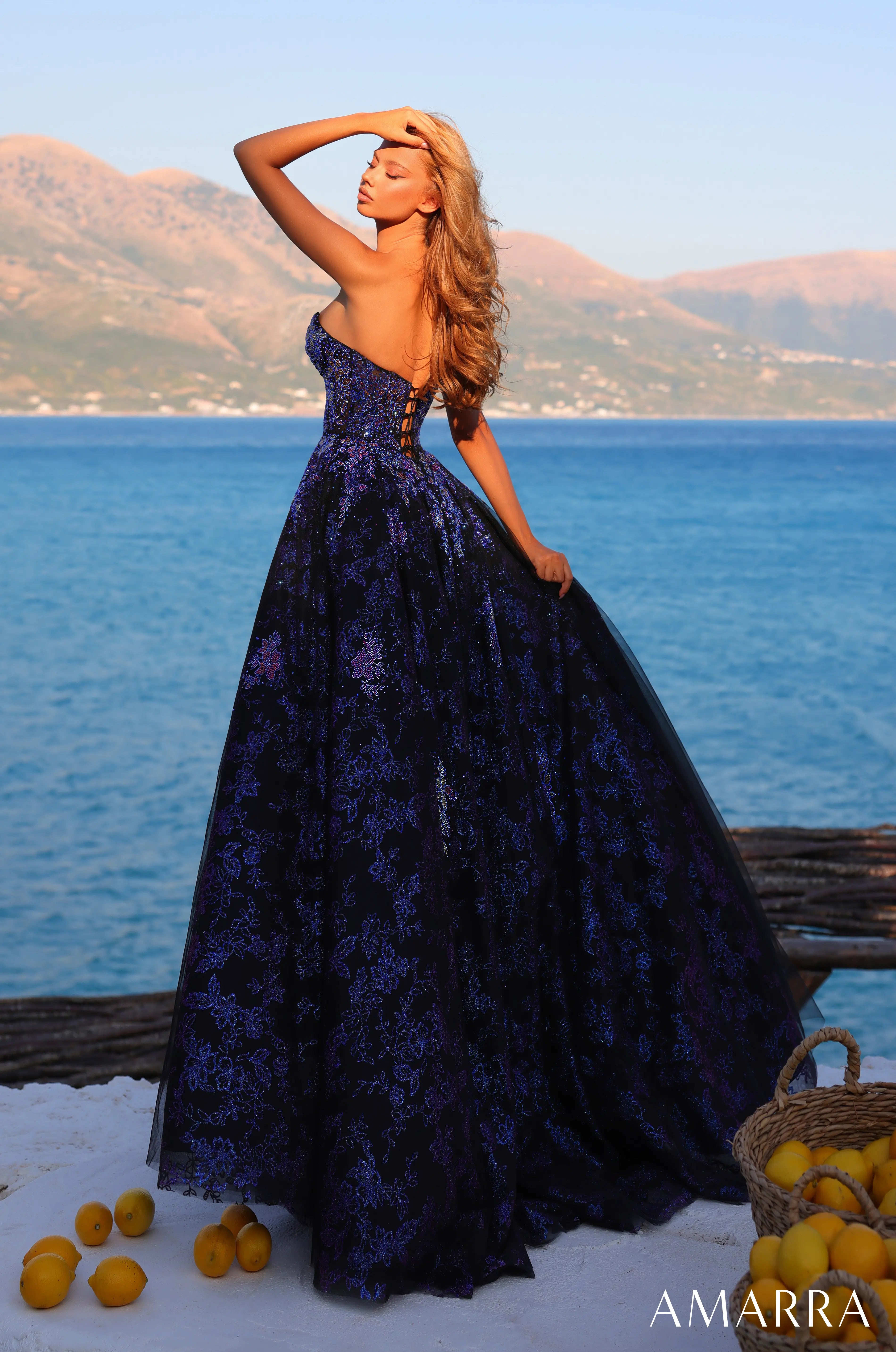 Woman in a purple evening gown by AMARRA standing by a scenic waterfront.