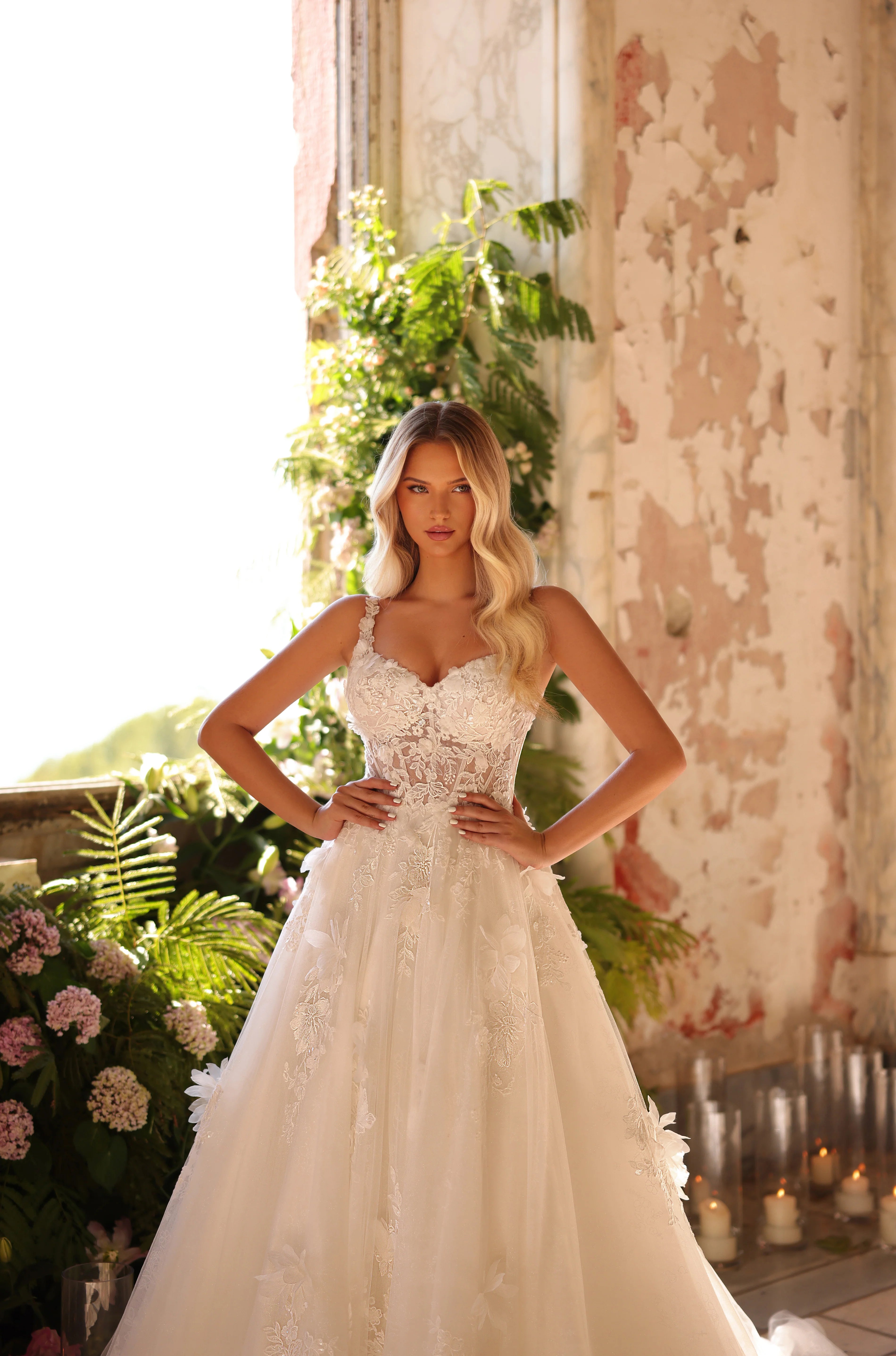 Woman in a white wedding dress standing in an outdoor setting with plants and candles.
