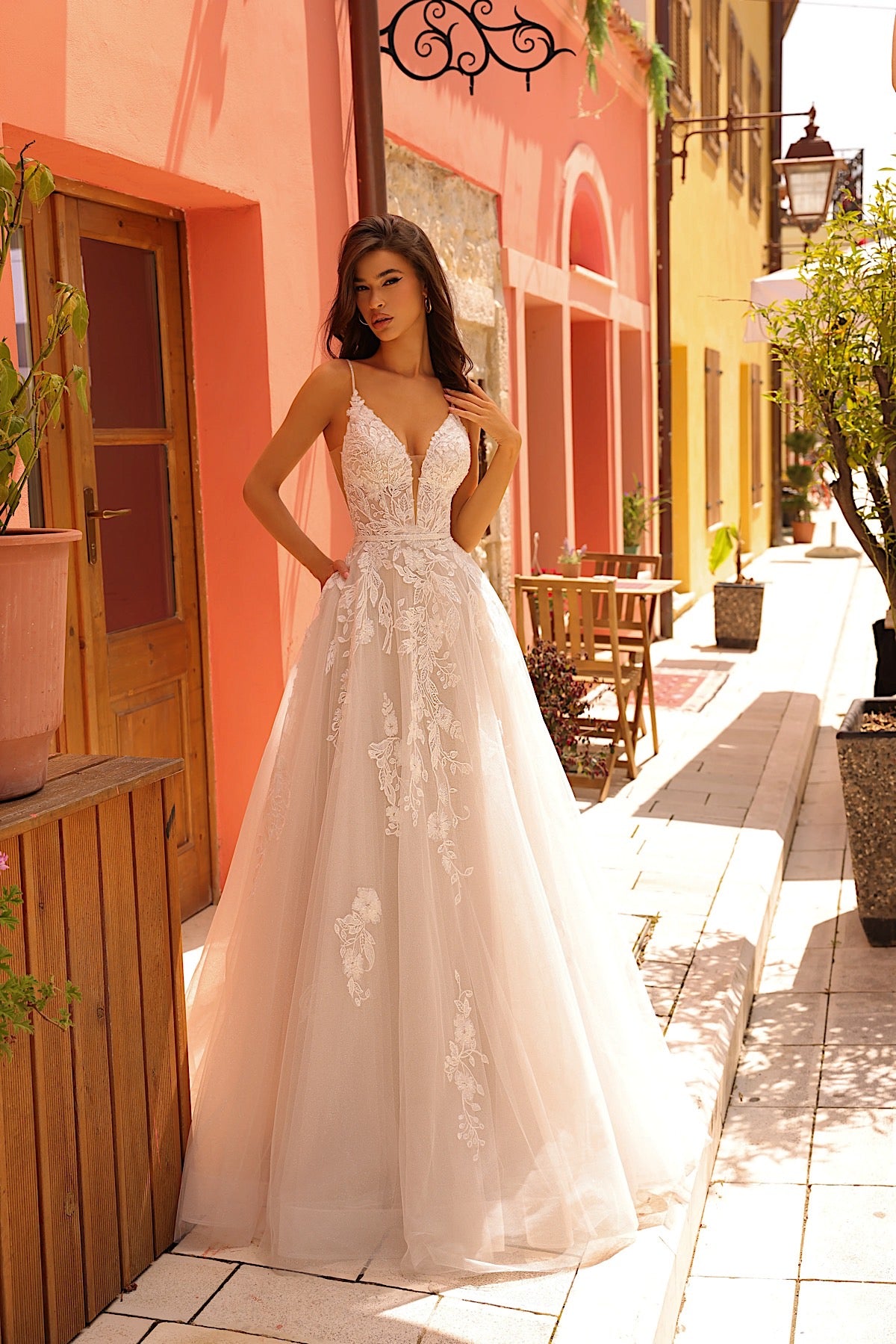 Woman in a white lace dress standing on a sunlit street with colorful buildings.