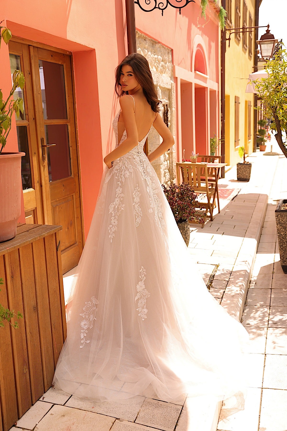Woman in a white lace dress standing on a street with colorful buildings.
