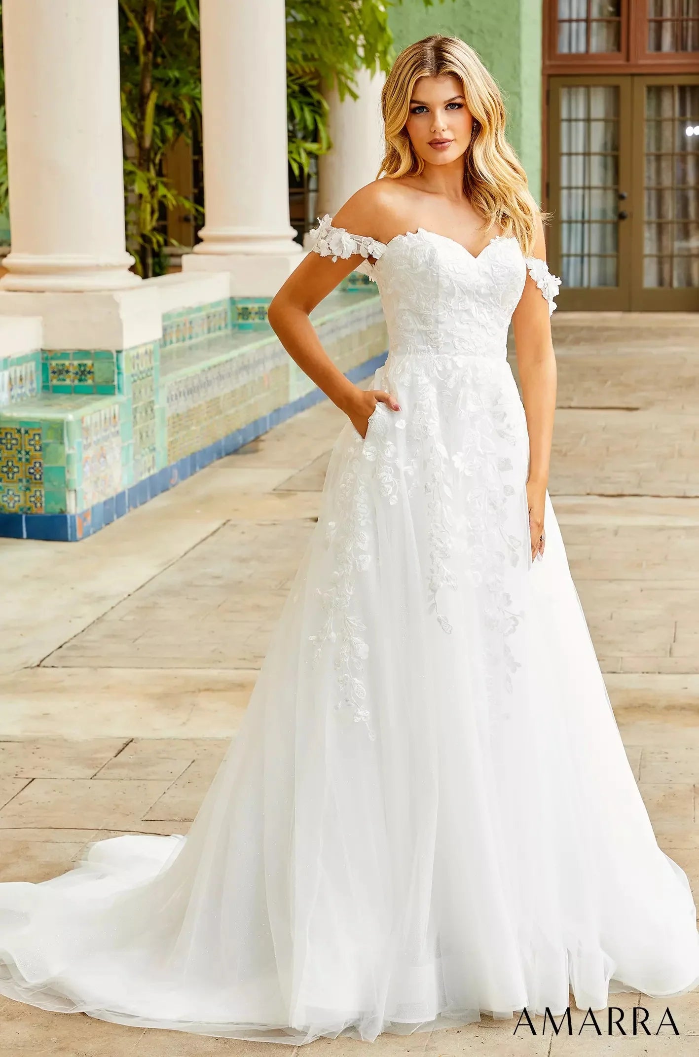 Woman in a white strapless gown standing outdoors with classical architecture in the background, with THE BRIDAL COMPANY branding.