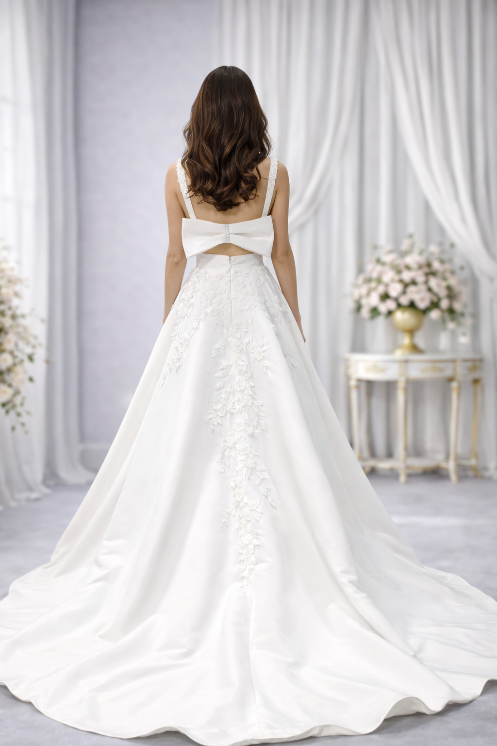 Woman in a white wedding dress with a floral back design, standing in a softly lit room.