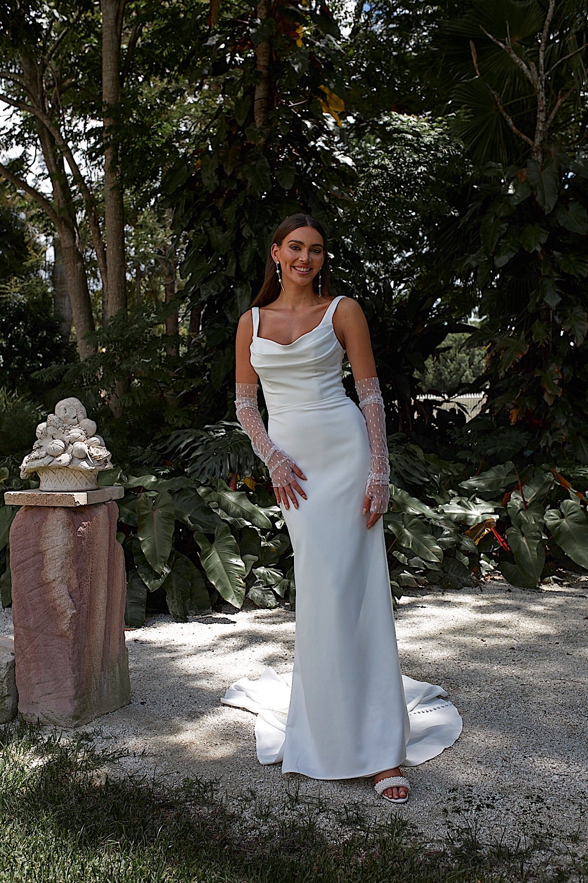 Woman in a white wedding dress standing outdoors with greenery in the background
