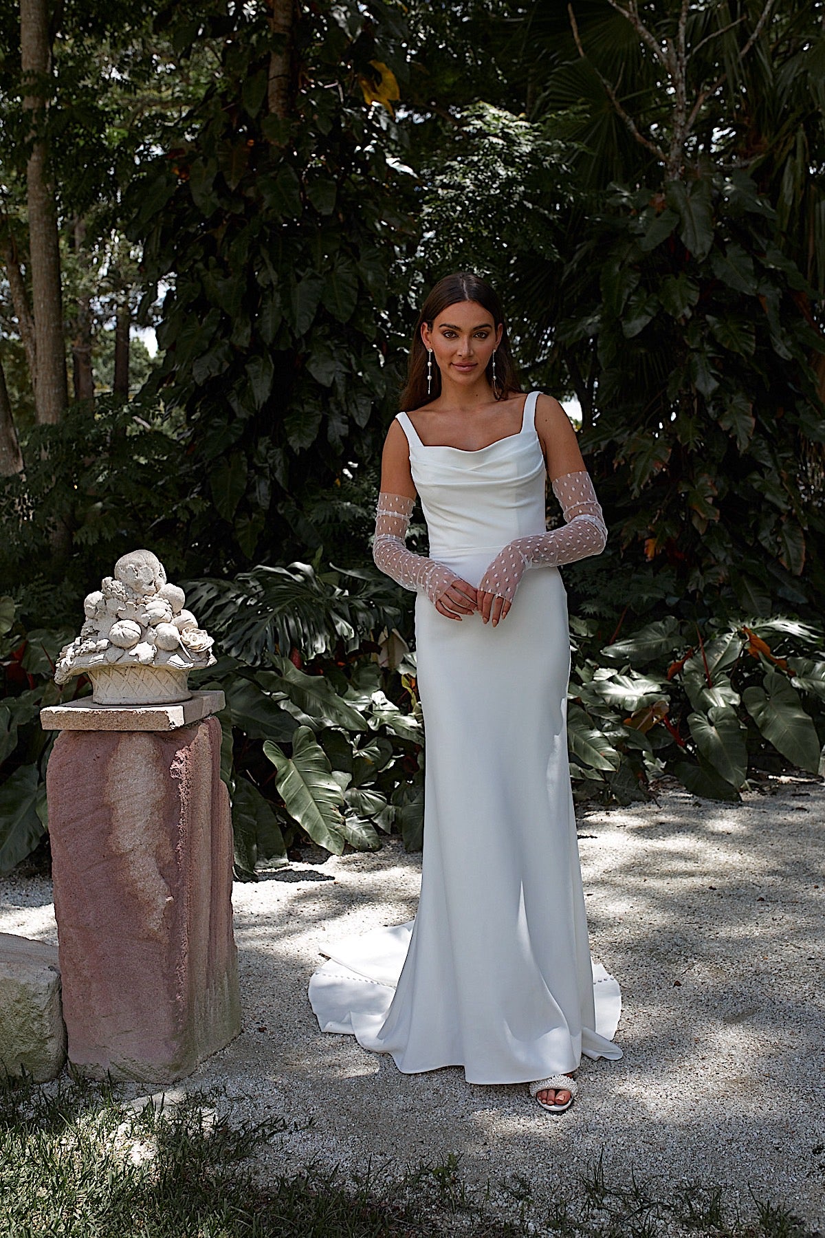 Woman in a white wedding dress standing in a natural setting with greenery.