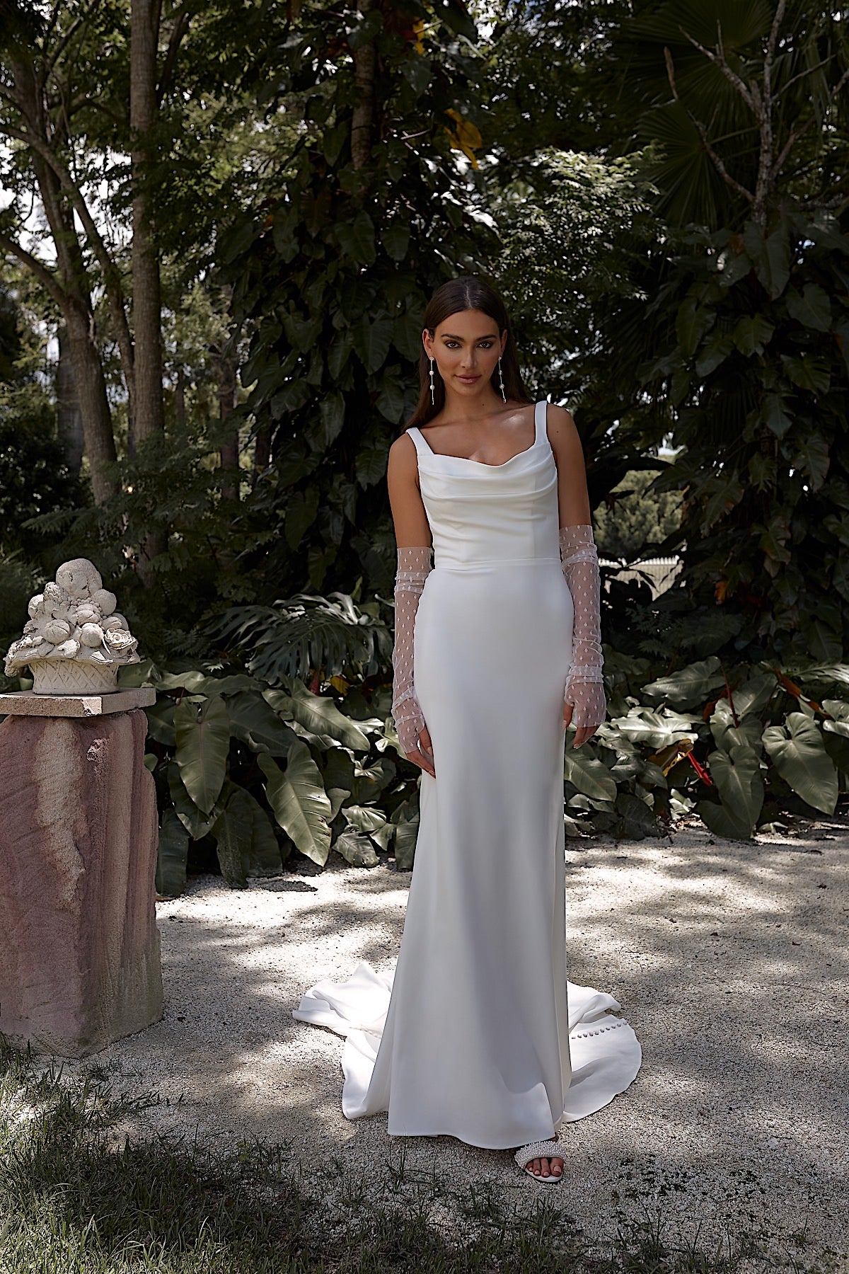 Woman in a white dress standing in a natural setting with trees and plants.