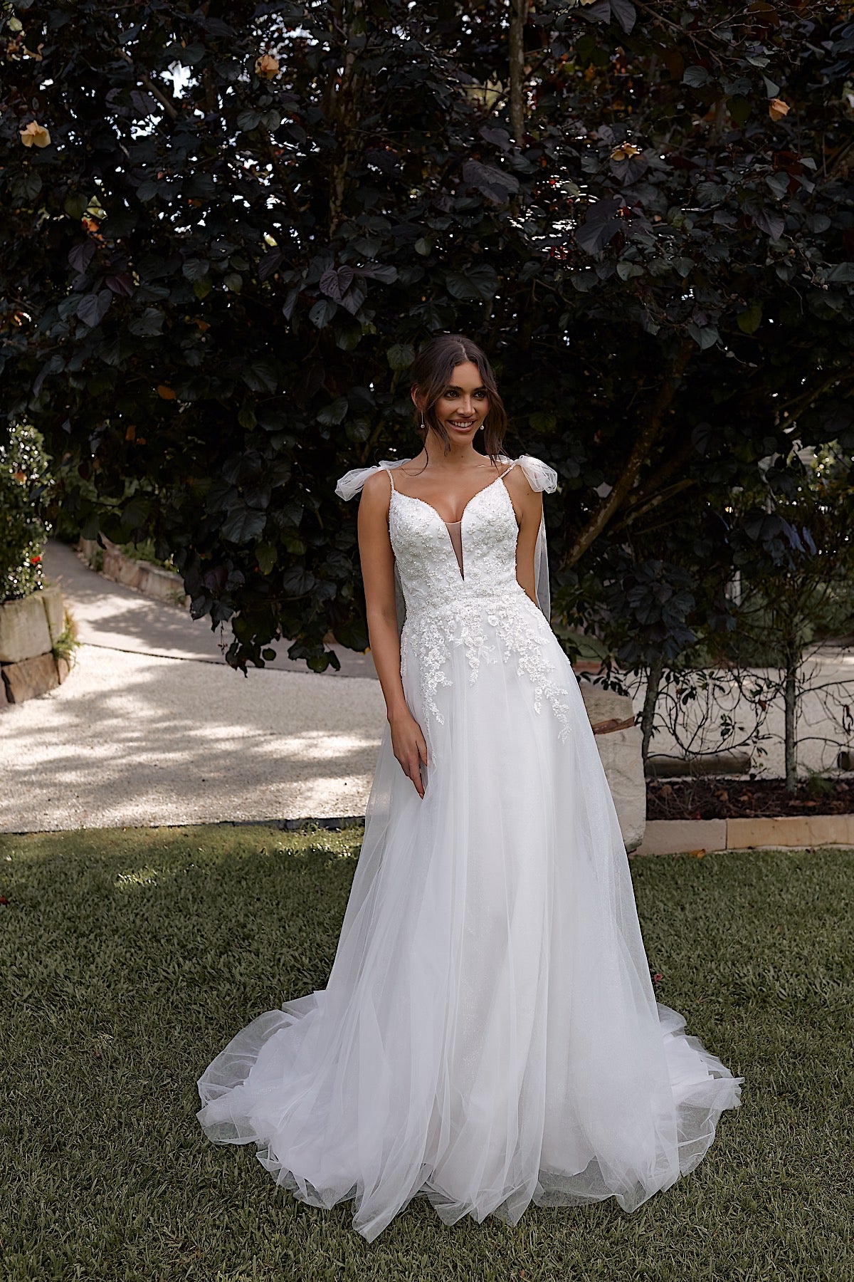 Woman in a white wedding dress standing outdoors with trees in the background
