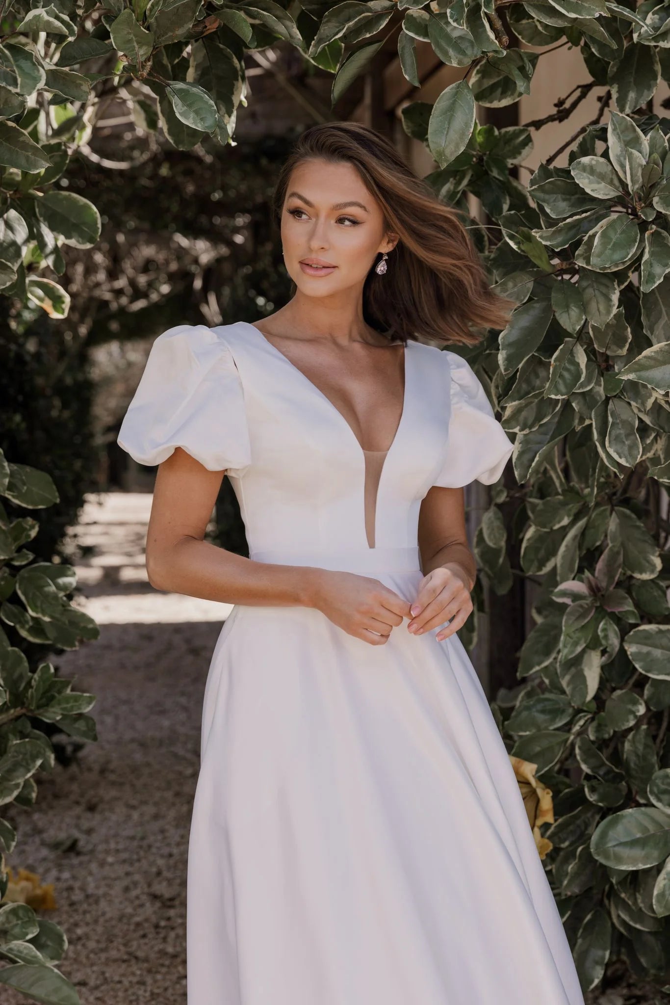 Woman in a white wedding dress standing among green foliage