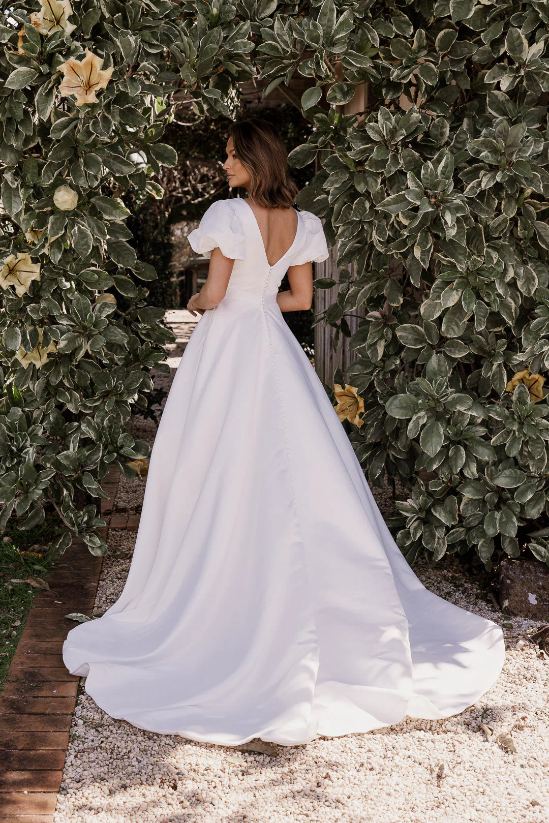 Woman in a white dress standing in front of green foliage