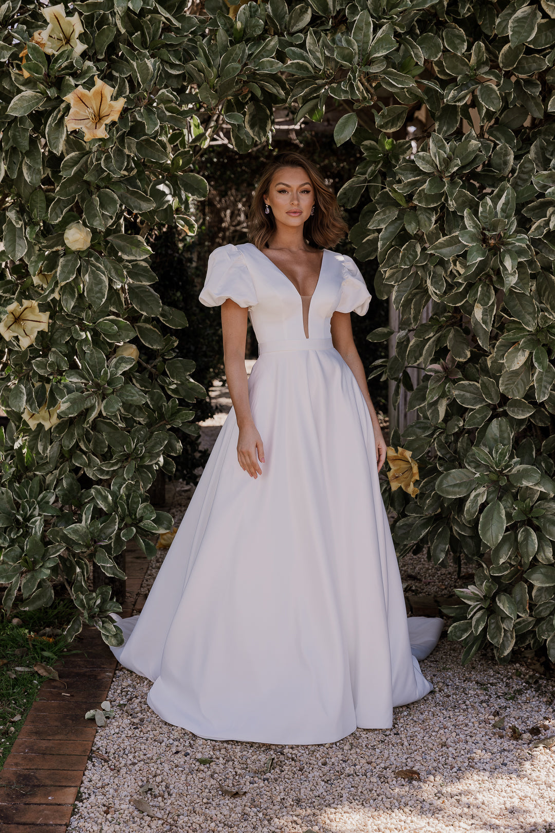 Woman in a white dress standing in front of green foliage