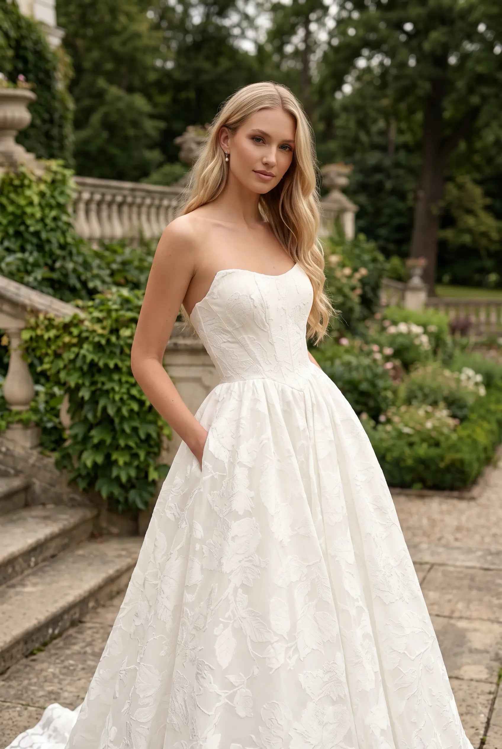 Embrace modern romance in this strapless floral jacquard wedding dress. Featuring a sculpted sweetheart corset bodice and a voluminous full skirt with a dramatic train. Shop the look today.